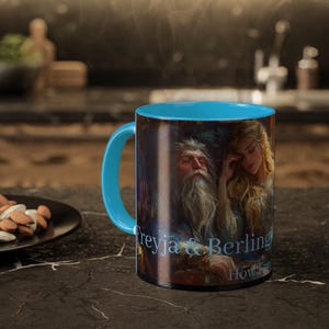 May include: A blue and black ceramic mug featuring a colourful image of a man and woman. The mug has the text "Freyja & Berling" and "How Far" printed on it.