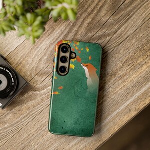 May include: A green phone case with a design of a fox gazing at falling leaves. The fox is orange and white, set against a textured green backdrop. The case has a camera module with three lenses.