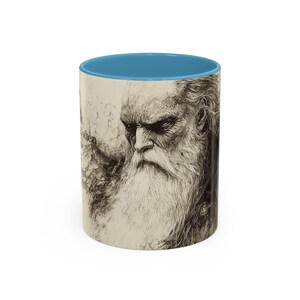 May include: A ceramic mug featuring a detailed black and white illustration of an elderly man with a long white beard and a blue interior. The mug has text on the side and is a unique gift idea.