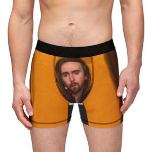 Peut inclure: Boxer orange avec une ceinture noire et une bordure noire. Le boxer présente une grande image du visage d'un homme sur le devant. Le boxer est fait d'une matière douce et confortable.