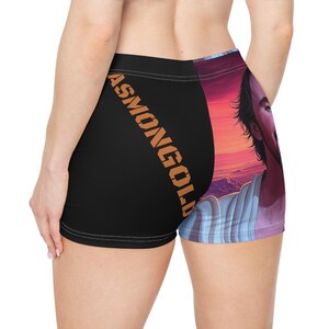 May include: Black and printed shorts with the word "ASMONGOLD" in orange diagonally across the left leg. The right leg features a portrait of a man with a sunset background.