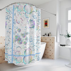 May include: A white shower curtain with a repeating pattern of large, colorful bubbles in shades of blue, green, and purple. The curtain has a light blue border and is hanging in a bathroom with a white tub and a curved shower rod.