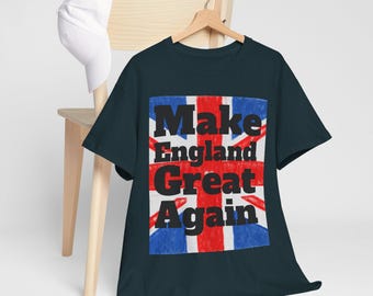 May include: Dark navy blue t-shirt with a graphic of the Union Jack flag and the words "Make England Great Again" in black. A white baseball cap rests on a wooden chair in the background.