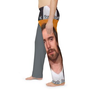 May include: Gray pajama pants with a colorful upper section and a large image of a person's face on the right leg. The upper section has the text "All Yeah Bro" in white letters on a black and orange background. The bottom of the right leg has the text "Yeah Bro".