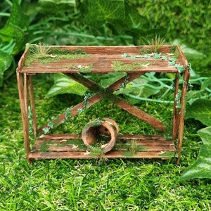 May include: A miniature wooden shelf with two levels, covered in moss and vines. The shelf is sitting on a bed of green artificial grass.