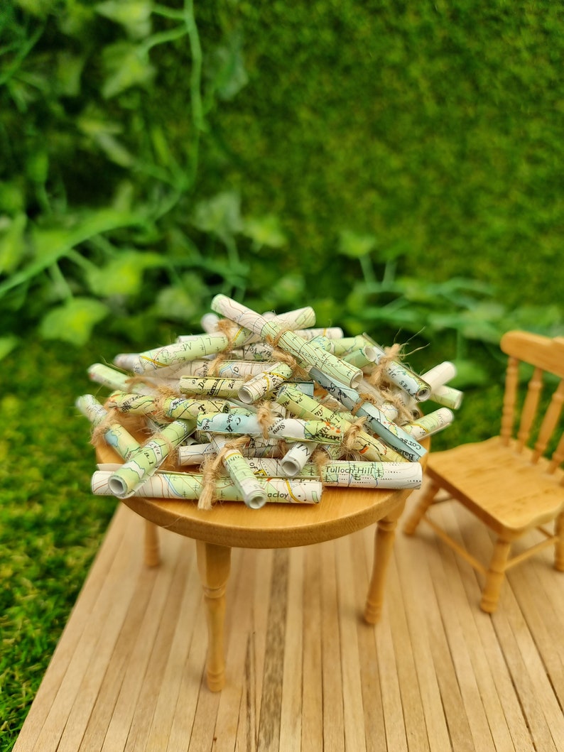 1:12 scale Miniature map scrolls tied with jute string are displayed on a miniature wooden table. The maps are mainly coloured white, green and blue