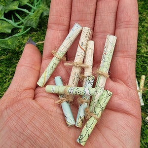 1:12 scale Miniature map scrolls tied with jute string are displayed in the palm of a hand. The maps are mainly coloured white, green and blue