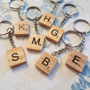 May include: A set of seven wooden letter tile keychains, each with a different letter and a corresponding point value. The letters are K, H, G, M, S, B, and E. The keychains are attached to silver key rings.