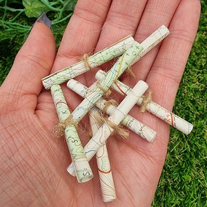 1:12 scale Miniature map scrolls tied with jute string are displayed in the palm of a hand. The maps are mainly coloured white, green and blue