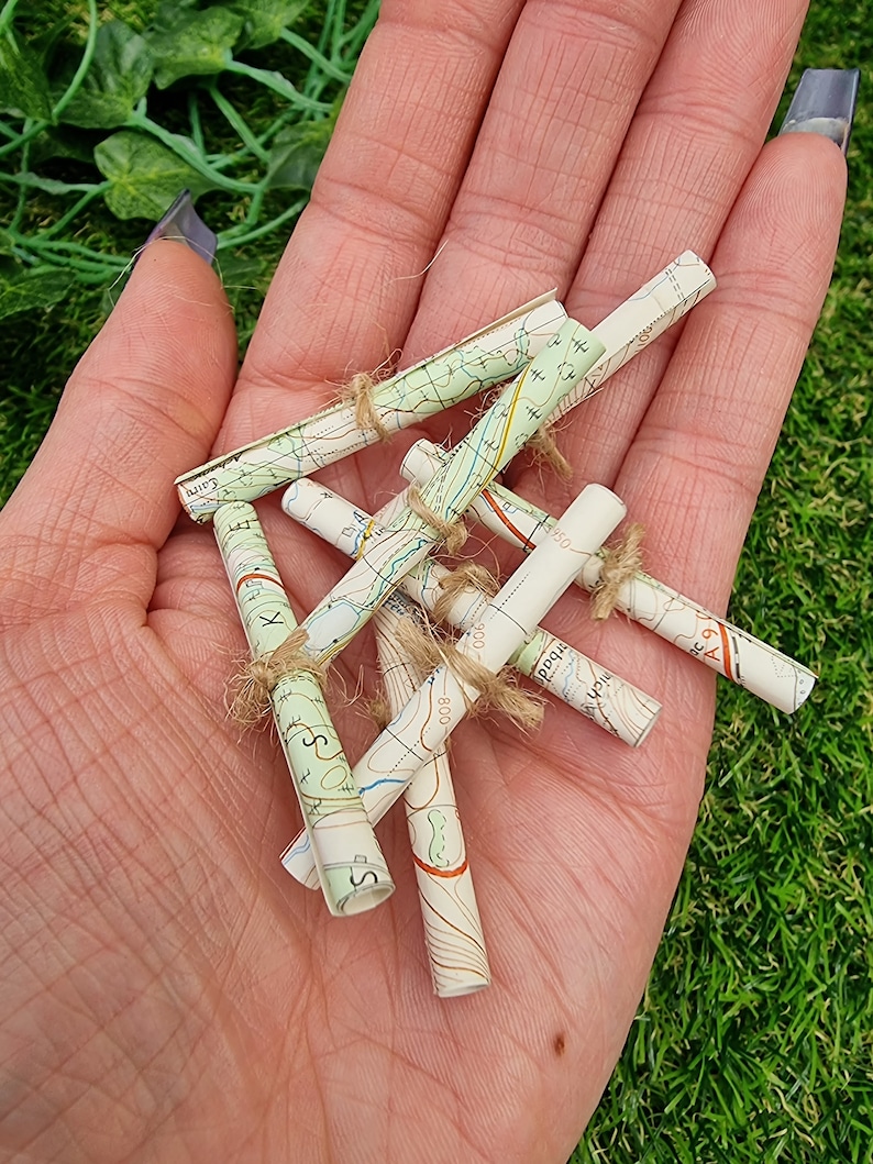 1:12 scale Miniature map scrolls tied with jute string are displayed in the palm of a hand. The maps are mainly coloured white, green and blue