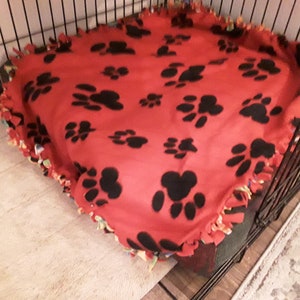 May include: Red fleece dog bed with black paw prints. The bed is in a black wire crate.