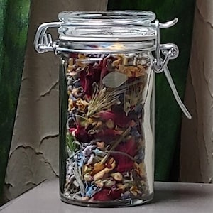 May include: A glass jar with a metal clasp lid filled with dried flowers and herbs. The flowers are red, yellow, and blue.
