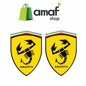 Op de afbeelding: Twee gele Abarth schildvormige emblemen met een zwart schorpioenontwerp en het woord "ABARTH" onderaan. De emblemen hebben een groene, witte en rode streep aan de bovenkant. De afbeelding bevat ook de tekst "amaf shop" en een groen winkelwagentas-pictogram.