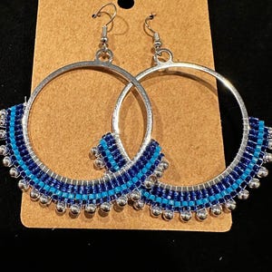 May include: A pair of silver hoop earrings with blue and turquoise beaded accents. The beads are arranged in a graduated pattern around the hoop.