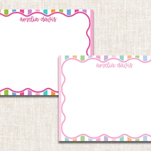 May include: Two personalized stationery cards with a white interior and a pink scalloped border. The border is outlined in a darker pink and is decorated with vertical stripes in various pastel colors. The name "Amelia Davis" is written in pink script.