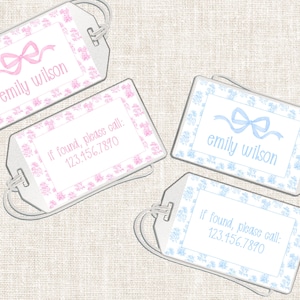 May include: Four luggage tags with a floral design and the text "emily wilson" and "If found, please call: 123.456.7890". Two tags have pink bows and text, and two have blue bows and text. Each tag has a silver-colored loop.