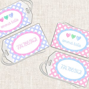 May include: Four personalized luggage tags with a white background, each with a different design. The tags feature a polka dot pattern in pink and blue, with an oval in the center. Some tags have the name "emma kate" and others have a phone number.