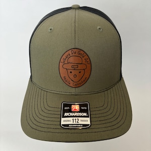 May include: A green and black trucker hat with a brown leather patch that says "Where Da Gold At?" with a cartoon leprechaun. The hat is adjustable and has the Richardson logo on the side.