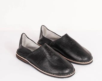 May include: A pair of black leather slip-on shoes with a simple design. The shoes have a rounded toe and a flat sole.