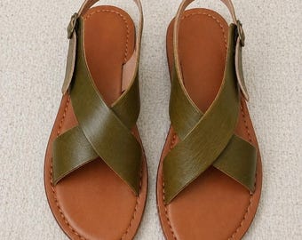 May include: A pair of olive green and brown leather sandals. The sandals have a criss-cross strap design across the foot and a buckle closure on the ankle strap. The soles are brown with visible stitching.