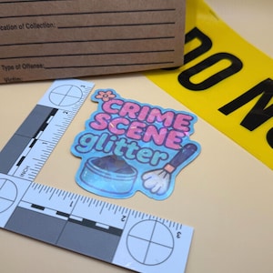 May include: A crime scene-themed sticker with the text "CRIME SCENE glitter" in pink and blue, featuring a makeup brush and a container of glitter. Also present are a brown evidence bag, a yellow "DO NOT CROSS" tape, and a forensic ruler.