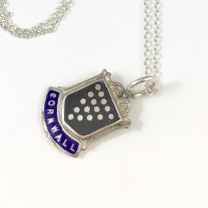 May include: A silver necklace with a pendant featuring a black shield design with white dots and the word "CORNWALL" in blue. The necklace chain is delicate and silver.