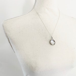 May include: A silver necklace with a round pendant. The pendant has a textured surface and a delicate design.