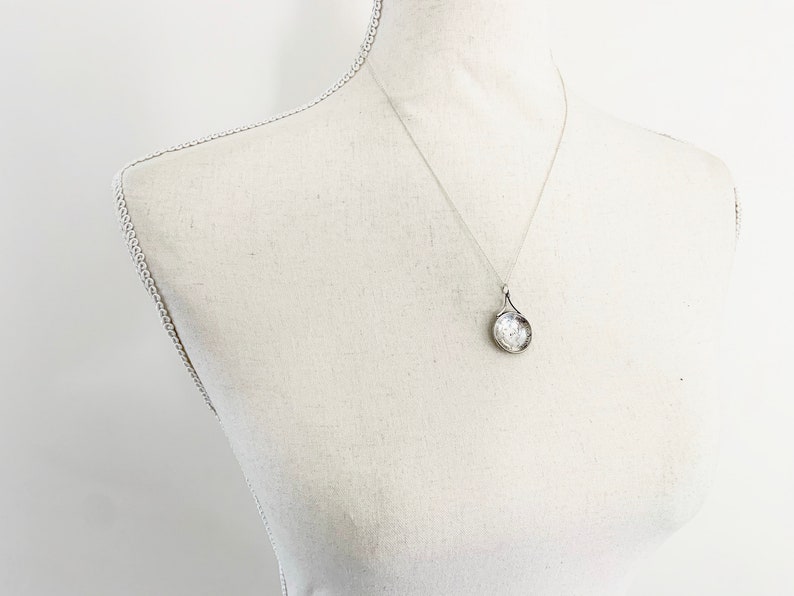 May include: A silver necklace with a round pendant. The pendant has a textured surface and a delicate design.