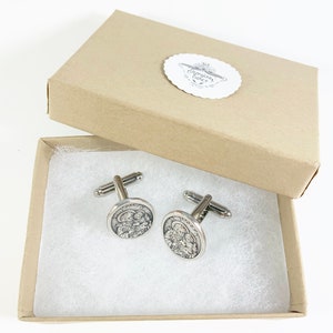 May include: A pair of silver cufflinks in a brown box. The cufflinks feature a circular design with a depiction of a family.