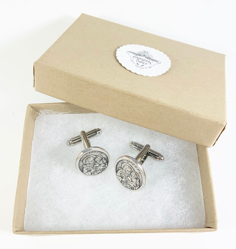 May include: A pair of silver cufflinks in a brown box. The cufflinks feature a circular design with a depiction of a family.