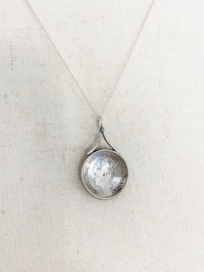 May include: Silver necklace with a pendant featuring a vintage Dutch coin with the inscription "KONINGIN DER NEDERLANDEN" and a profile of Queen Wilhelmina.