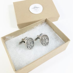 May include: A pair of silver cufflinks with a religious image of the Holy Family in a brown gift box.