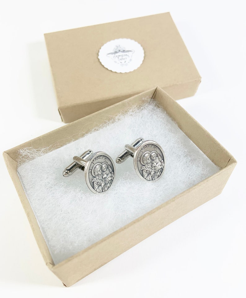 May include: A pair of silver cufflinks with a religious image of the Holy Family in a brown gift box.