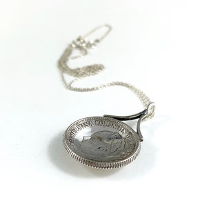 May include: A silver necklace with a coin pendant featuring a profile of Queen Wilhelmina of the Netherlands. The coin is inscribed with "WILHELMINA KONINGIN DER NEDERLANDEN".