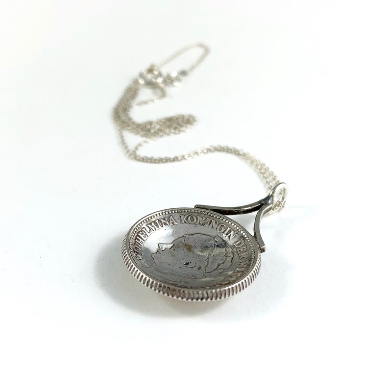 May include: A silver necklace with a coin pendant featuring a profile of Queen Wilhelmina of the Netherlands. The coin is inscribed with "WILHELMINA KONINGIN DER NEDERLANDEN".