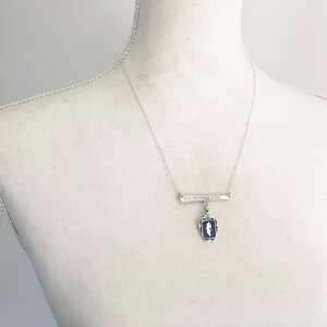 May include: A silver-toned necklace with a bar pendant and a rectangular blue and white pendant. The bar pendant has engraved text. The necklace is displayed on a mannequin.