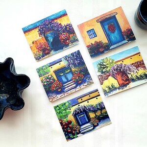 May include: Set of five colorful greeting cards featuring illustrations of adobe style houses with blue doors and blooming flowers. The cards are perfect for sending a special message to someone you care about.