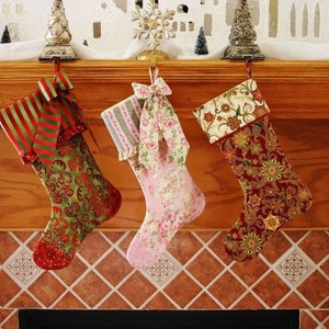 Puede incluir: Tres calcetines navideños cuelgan de una repisa de madera. Los calcetines presentan patrones festivos en rojo, verde y rosa, con lazos decorativos. La repisa está adornada con decoraciones navideñas en miniatura.