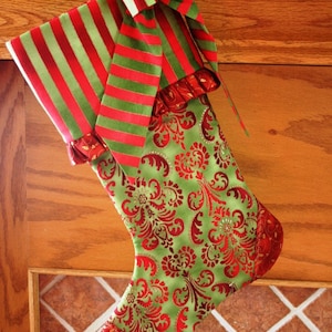 May include: A green and red Christmas stocking with a red and green striped bow. The stocking has a red and gold floral pattern.