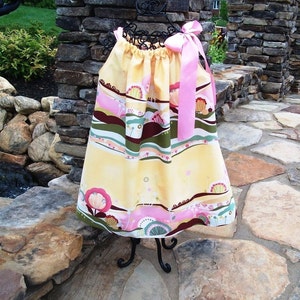 May include: A yellow and pink dress with a floral and landscape print. The dress has a pink ribbon tied around the neck.