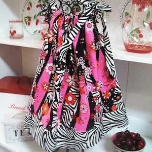 May include: A pink and black zebra print dress with a floral pattern. The dress is on a black stand and has a ruffled hem.