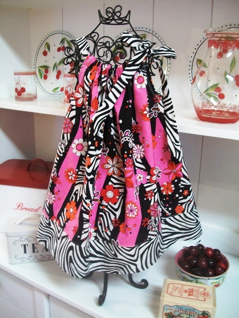 May include: A pink and black zebra print dress with a floral pattern. The dress is on a black stand and has a ruffled hem.