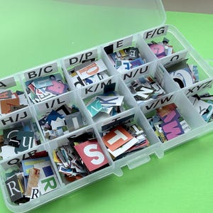 May include: A clear plastic organiser filled with colourful paper letters and letter fragments. The organiser is divided into labelled compartments, including A, B/C, D/P, E, F/G, H/J, I/L, K/M, N/U, V/W, and XYZ. The background is a solid green.