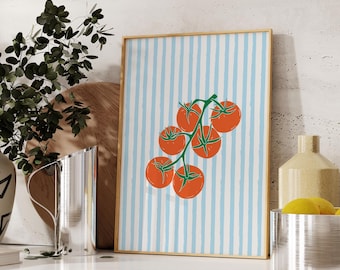 May include: A framed print with a design of orange tomatoes on a green stem, set against a light blue and white striped backdrop. The artwork is displayed on a white countertop with other decorative items.