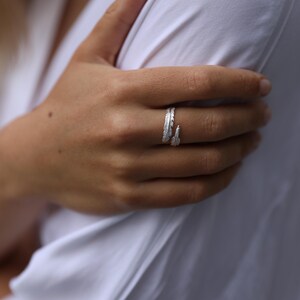 Può includere: Un anello d'argento con un design a forma di piuma. L'anello è indossato sul dito medio di una mano.
