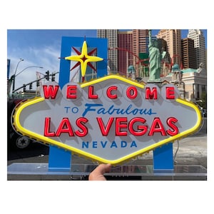 以下が含まれることがあります： Welcome to Fabulous Las Vegasの看板のレプリカ。白い背景に赤い文字、黄色のネオン風の縁取り、青い星の飾りが付いています。看板にはWelcome to Fabulous Las Vegas Nevadaという文字が表示されています。