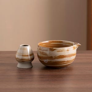 May include: Two ceramic bowls with a brown and white marbled glaze. The larger bowl has a pouring spout. The bowls are sitting on a wooden surface.