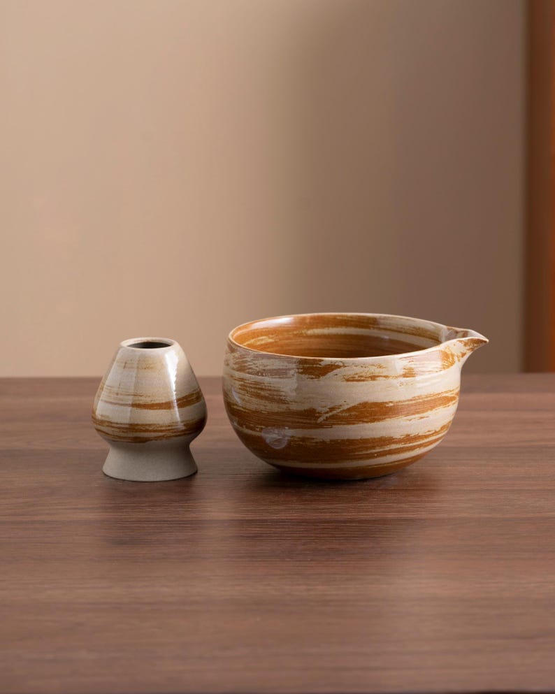 May include: Two ceramic bowls with a brown and white marbled glaze. The larger bowl has a pouring spout. The bowls are sitting on a wooden surface.