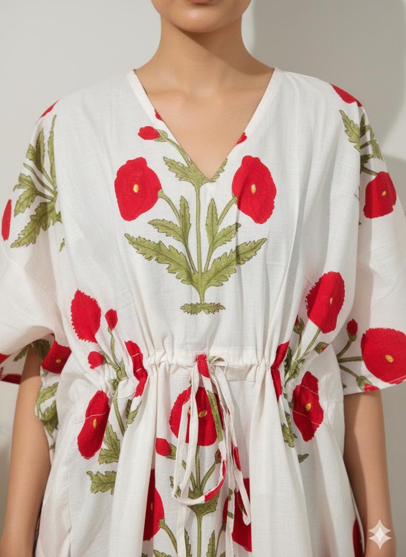 K&ouml;nnte beinhalten: Wei&szlig;es Kaftan-Kleid mit rotem Blumendruck. Das Kleid hat eine Taille mit Kordelzug und kurze &Auml;rmel. Das florale Design umfasst rote Mohnblumen und gr&uuml;ne Bl&auml;tter.