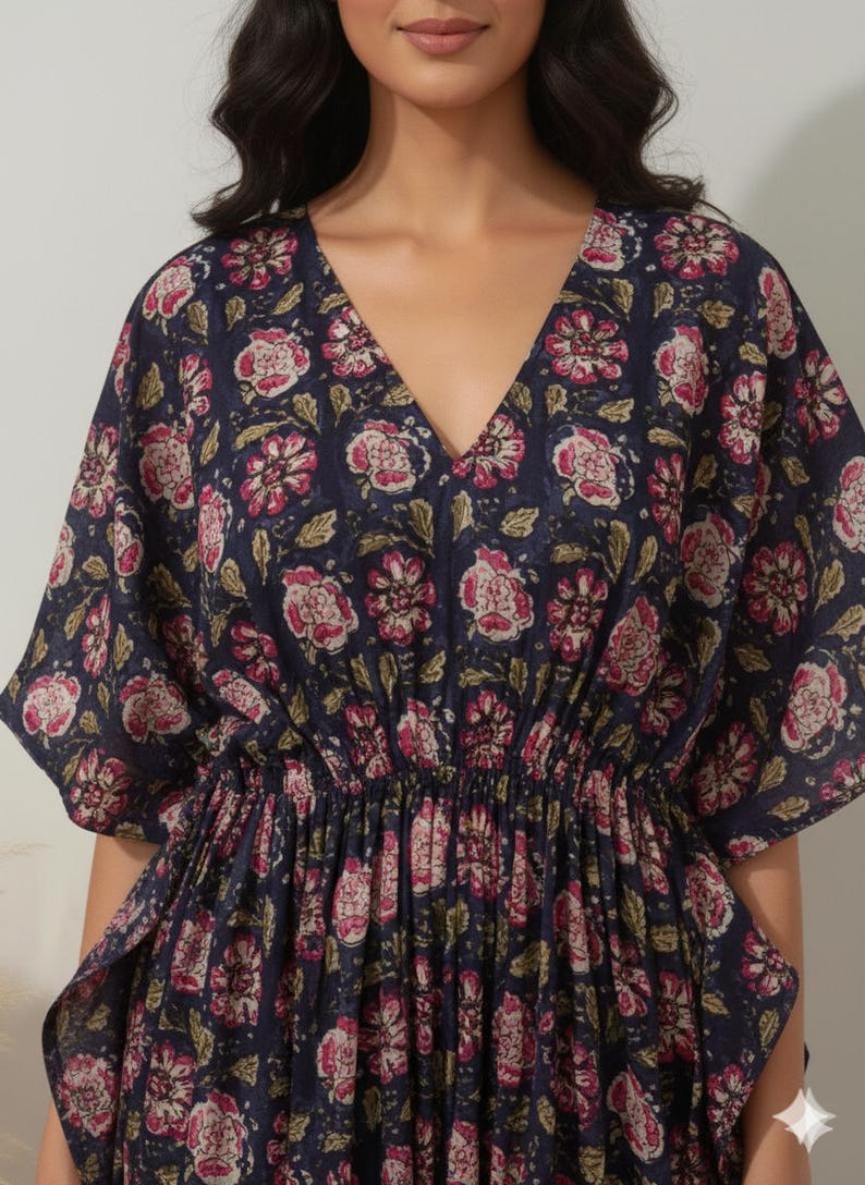 K&ouml;nnte beinhalten: Marineblaues Kaftan-Kleid mit V-Ausschnitt und floralem Muster in Rosa und Wei&szlig;. Das Kleid hat kurze &Auml;rmel und eine geraffte Taille. Der Blumendruck enth&auml;lt gr&uuml;ne Bl&auml;tter. Das Kleid ist aus leichtem Stoff gefertigt.